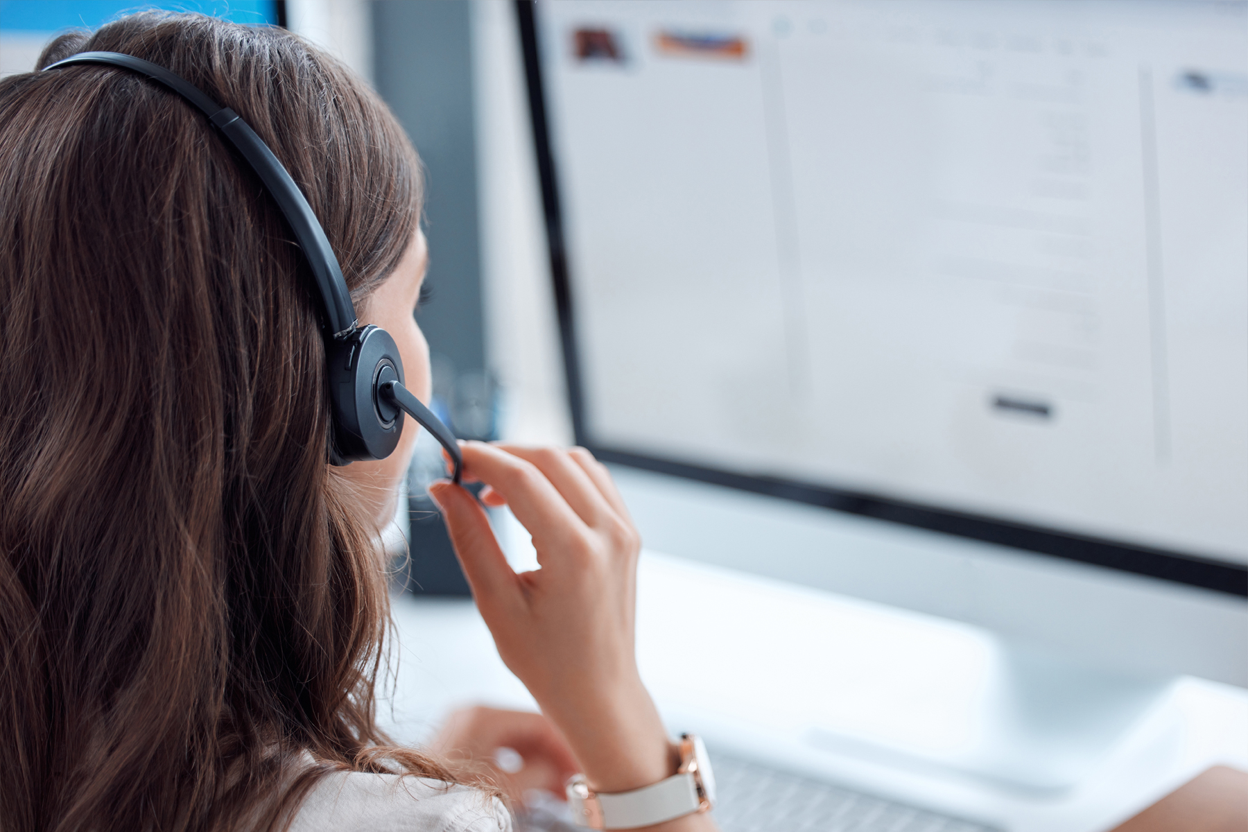 Dunkelhaarige Frau mit Headset vor einem Monitor